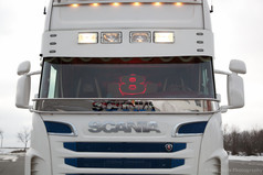 Beleuchtetes Scheibengitter mit roter Ziffer 8 hinter der Windschutzscheibe eines wei�en Scania LKWs.