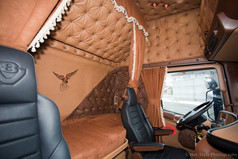 Braune Bettgardine mit wei�er Borte im LKW-Fahrerhaus, umgeben von gesteppter brauner Polsterung.