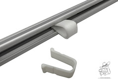 Wei�er U-f�rmiger Feststeller f�r Gardinenschiene, teilweise in silberner Schiene eingesetzt, ein weiterer liegt daneben.