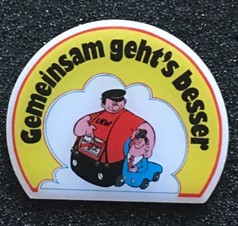Scandi Pin mit Cartoon-Motiv: Gro�er Mann im LKW-Shirt hilft kleinem Mann im blauen Auto. Text: Gemeinsam geht