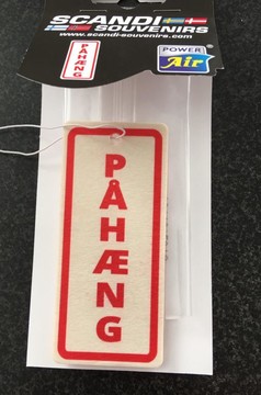 Rechteckiger cremefarbener Lufterfrischer mit rotem Rand und der Aufschrift PAH�NG, in transparenter Verpackung mit wei�er Schnur.