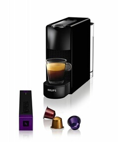 Schwarze Nespresso Essenza Mini Kaffeemaschine von Krups mit einer Tasse Espresso, mehreren Kapseln und Kapselpackung.