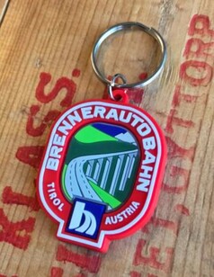 Roter Schl�sselanh�nger aus Gummi mit Brennerautobahn-Motiv, Br�cke und Bergen. Beschriftet: "Brennerautobahn Tirol Austria".