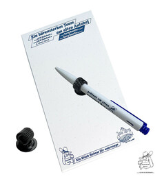 Wei�er Notizblock "Ein b�renstarkes Team" mit Kugelschreiber "geklaut im Autohof Berg" und schwarzen Klebeclips.