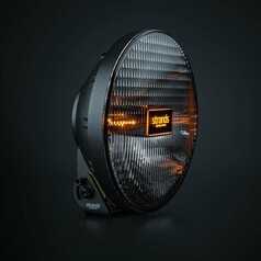 Runder Strands Fernscheinwerfer IZE LED OG 9, schwarz, mit gerippter Linse und leuchtendem bernsteinfarbenem Strands Logo.