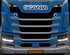 Front eines blauen Scania LKW mit eingeschalteten Tagfahrlicht-LEDs und beleuchtetem Scania-Schriftzug.